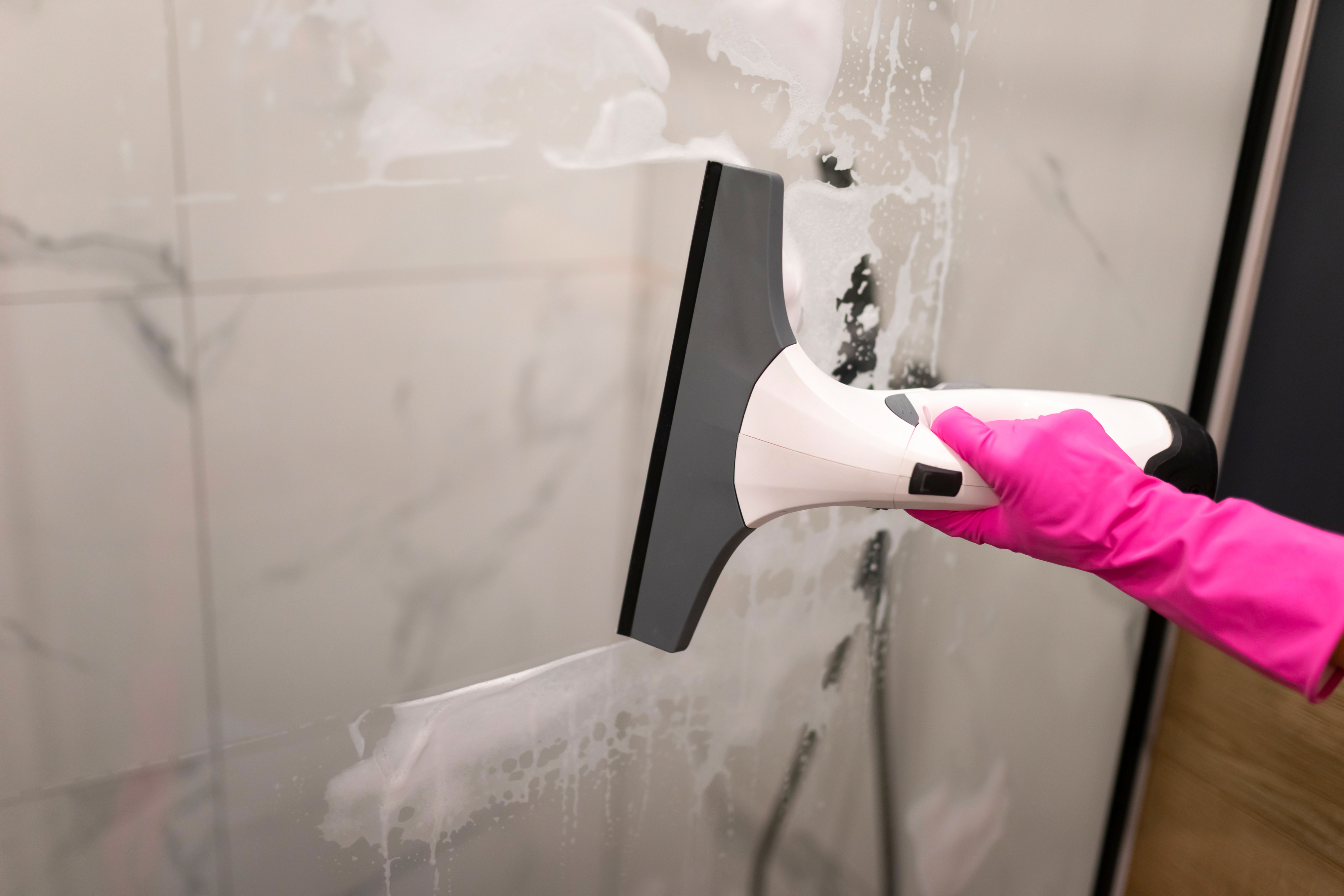 Hand in pink glove cleans a marble surface with a white and black squeegee