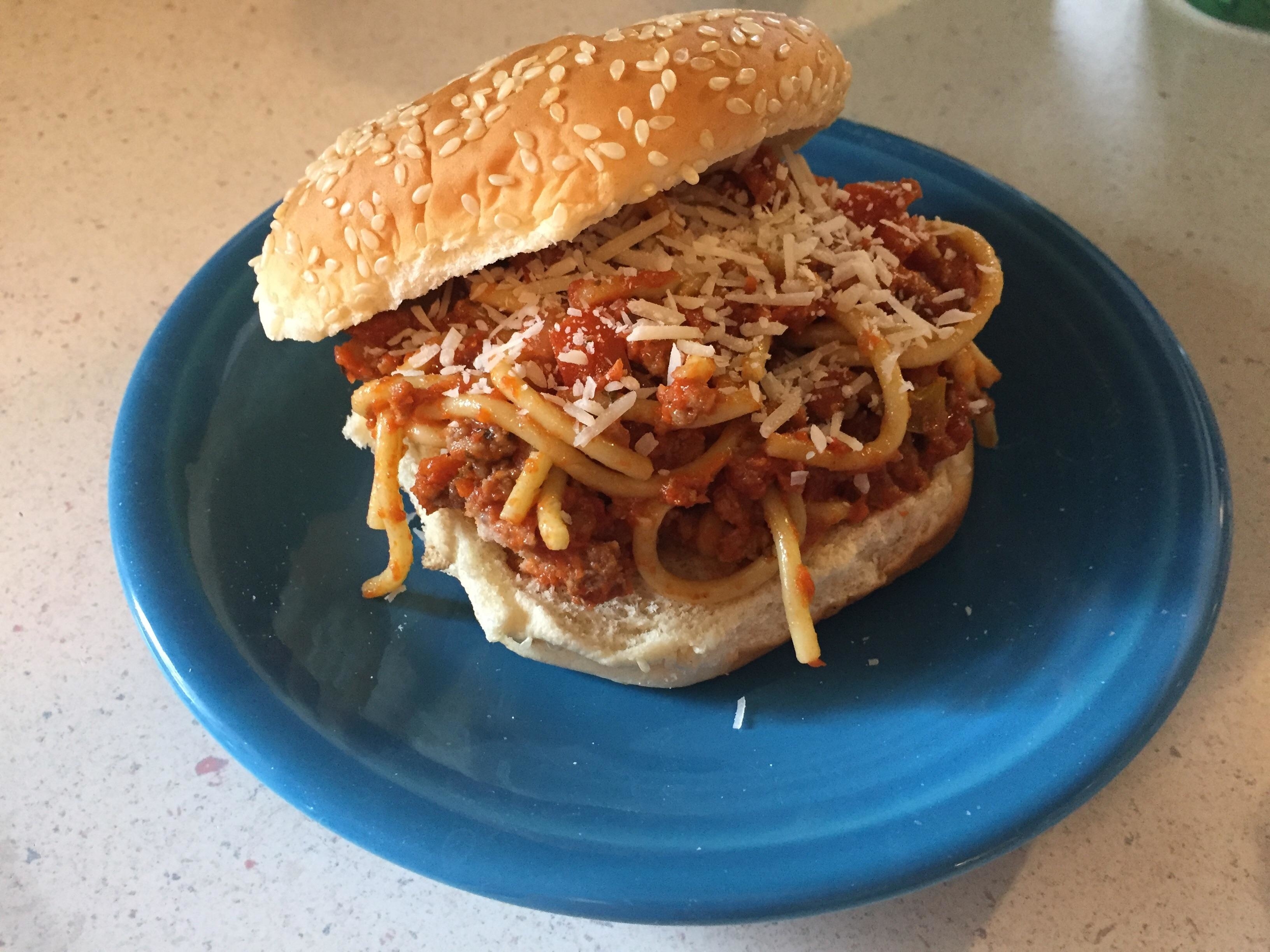 A spaghetti sandwich with meat sauce and shredded cheese on a sesame seed bun, served on a blue plate