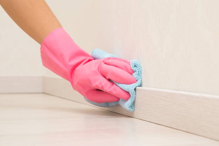 Hand in pink glove cleaning a baseboard with a blue cloth