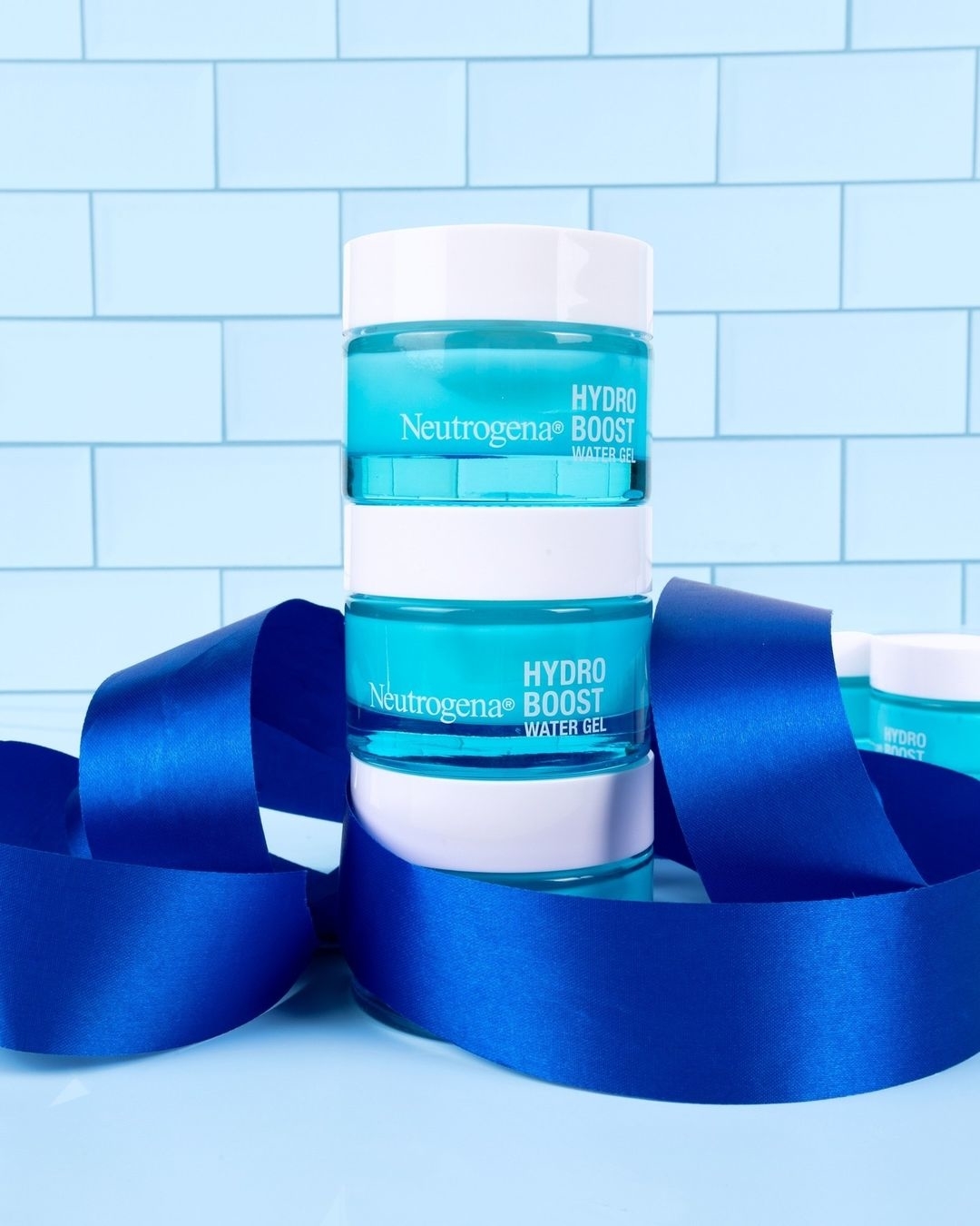 Neutrogena Hydro Boost moisturizer jars wrapped with a blue ribbon against a blue-tiled background