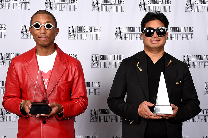Two people standing with awards; one wears a red jacket and the other a black jacket with gold detailing