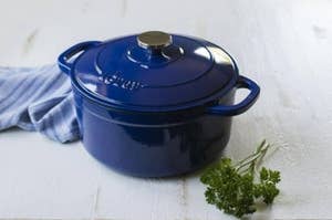A blue enameled cast iron Dutch oven on a white wooden surface, beside a sprig of parsley