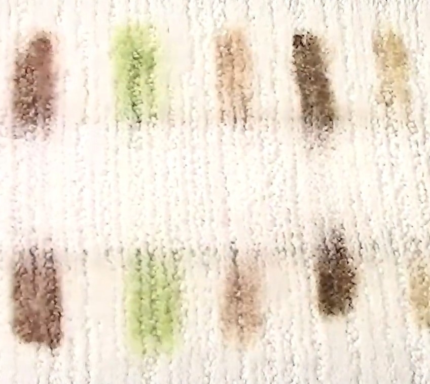 A white textured rug with a row of stains on it, partially removed to show the effectiveness of a stain remover spray
