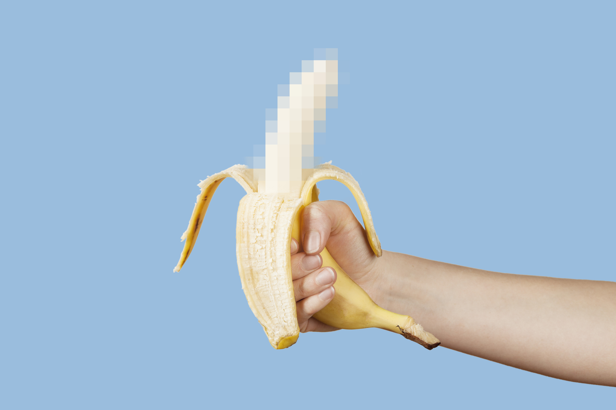Hand holding a banana with the top portion pixelated, suggesting a censored object