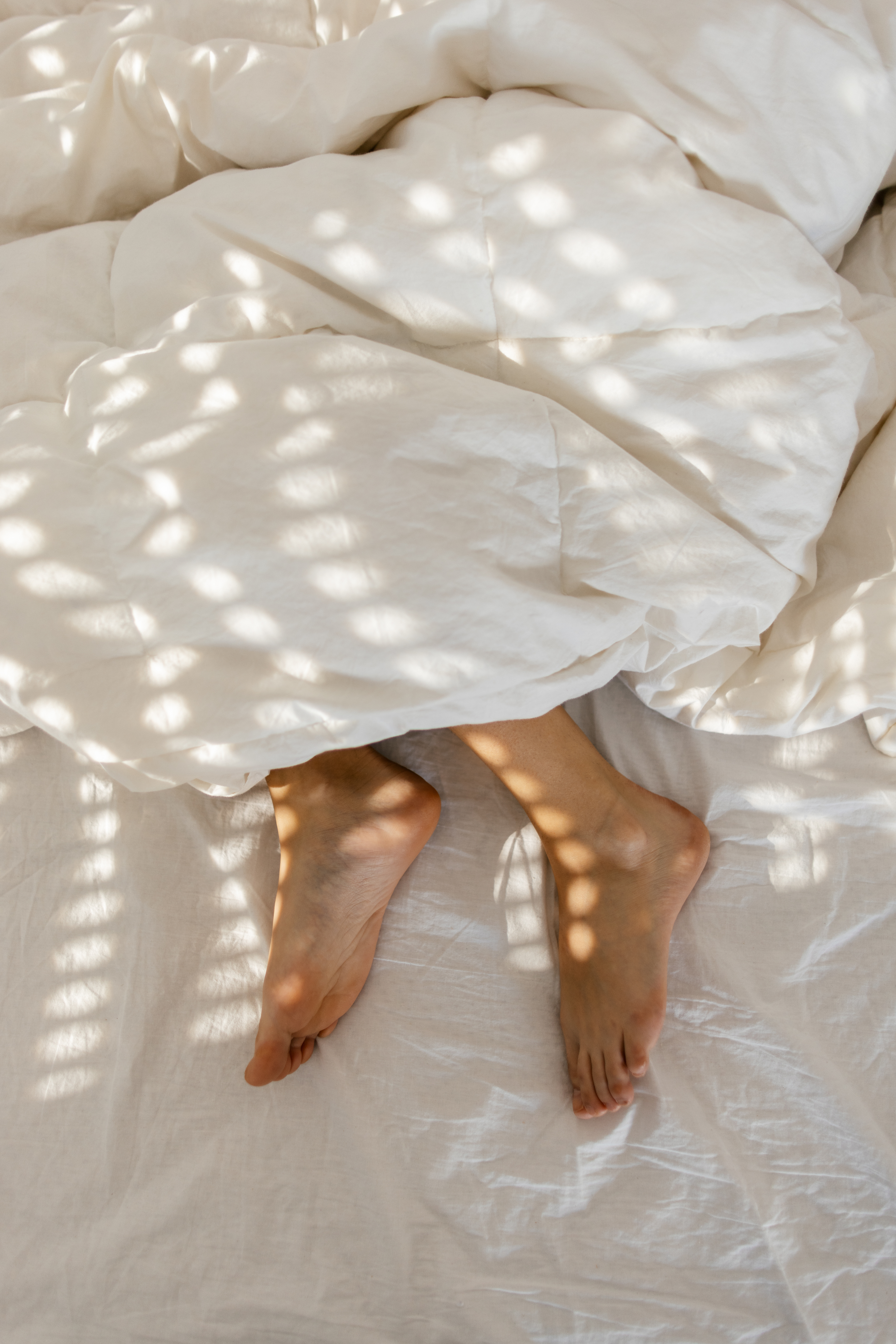 Person&#x27;s bare feet sticking out from under a light blanket with sunlight filtering through