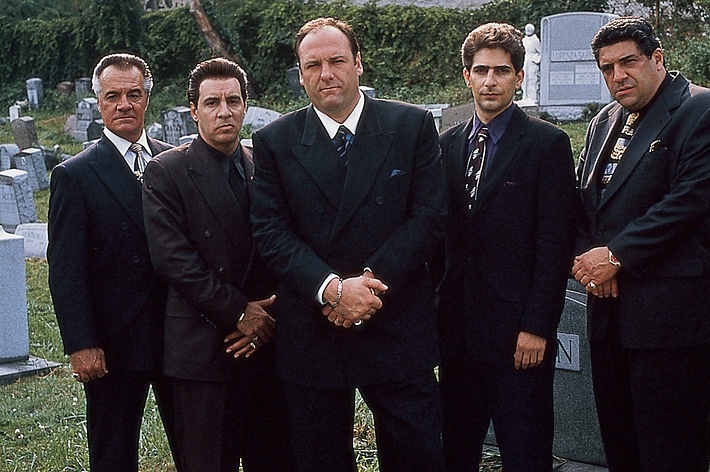 Five men dressed in dark suits and ties standing solemnly in a cemetery