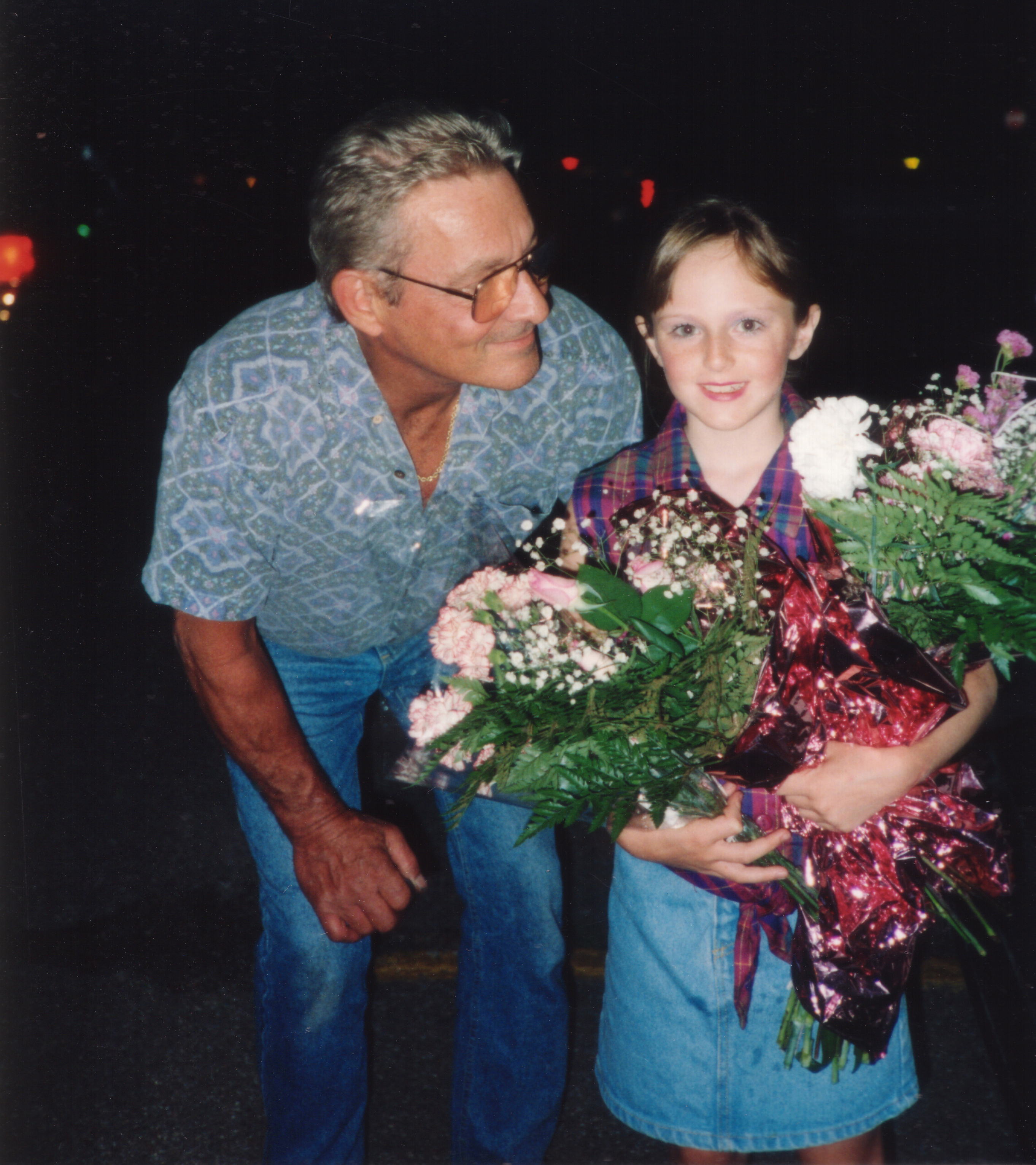 Older man in glasses smiling at young girl holding flowers. They stand close, sharing a happy moment