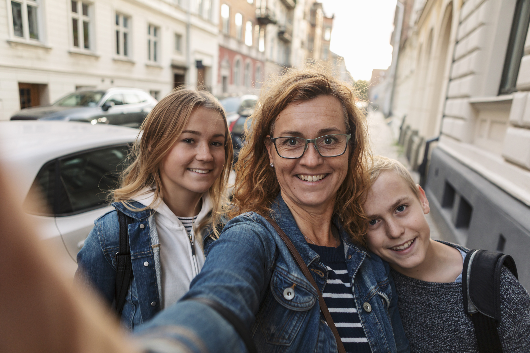 Three people in a selfie, two young and one middle-aged, smiling on a city street