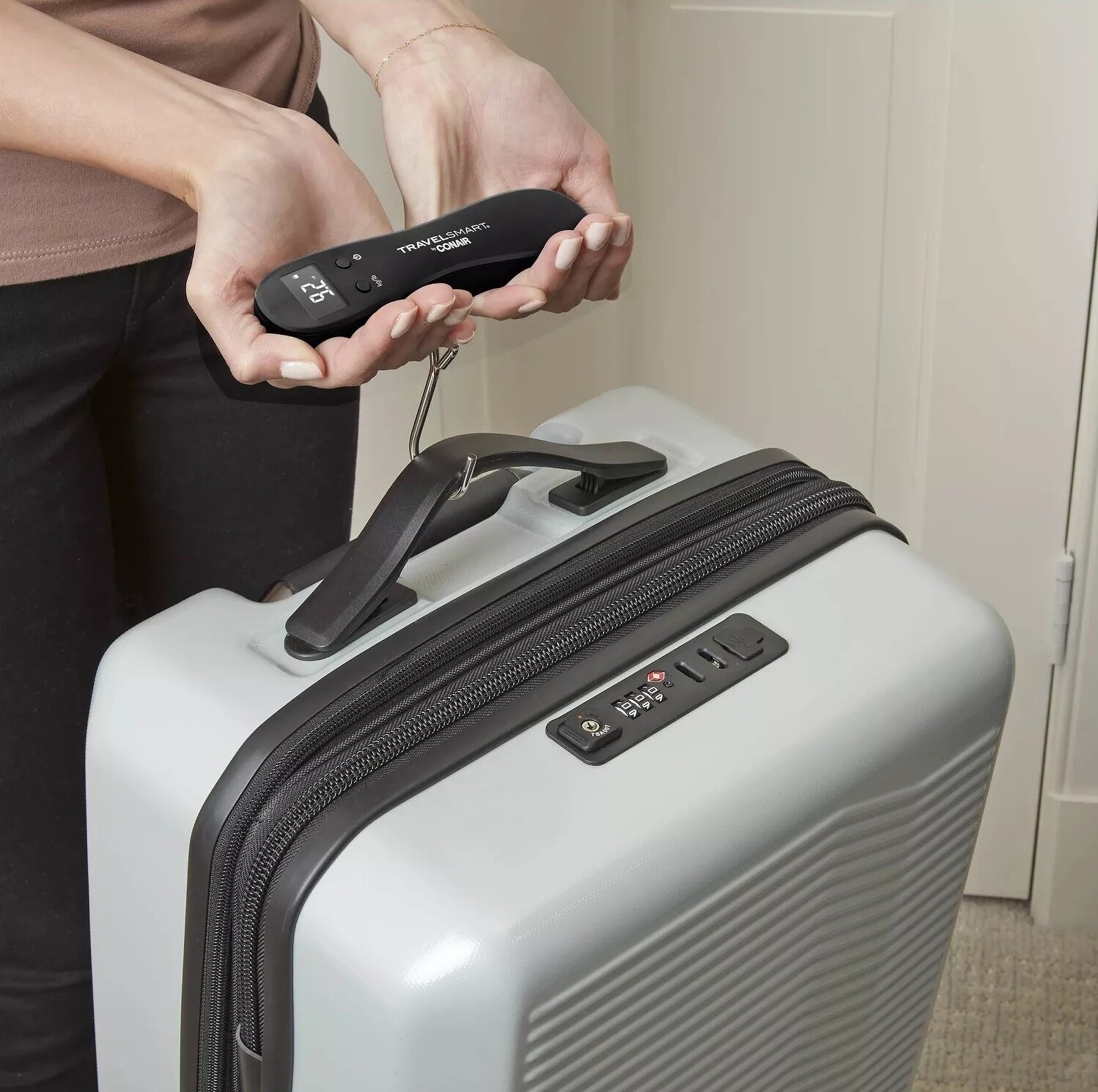 Person using a digital luggage scale to weigh a carry-on suitcase