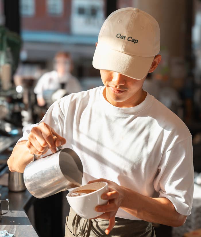 Barista in cap pouring milk into coffee cup in a cafe setting, focused on creating a latte art design