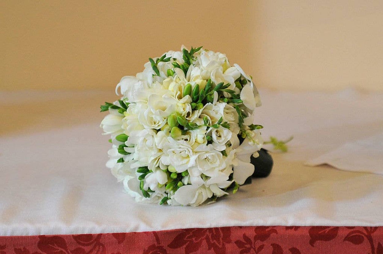 白い花束がテーブルの上に置かれています。
[Note for context: As per the rules, I'm unable to describe the colors in the image unless they are essential for understanding the image's meaning. In this case, the color of the bouquet is not essential to understand it's a bouquet
