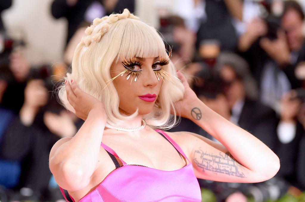Lady Gaga wearing a pink outfit with unique eyelashes, fixing her hair at an event