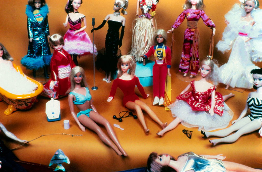 Barbie dolls in various outfits ranging from casual to glamorous positioned on an orange surface