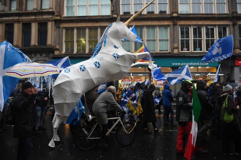 Protesters with large unicorn puppet amongst Scottish flags on a city street