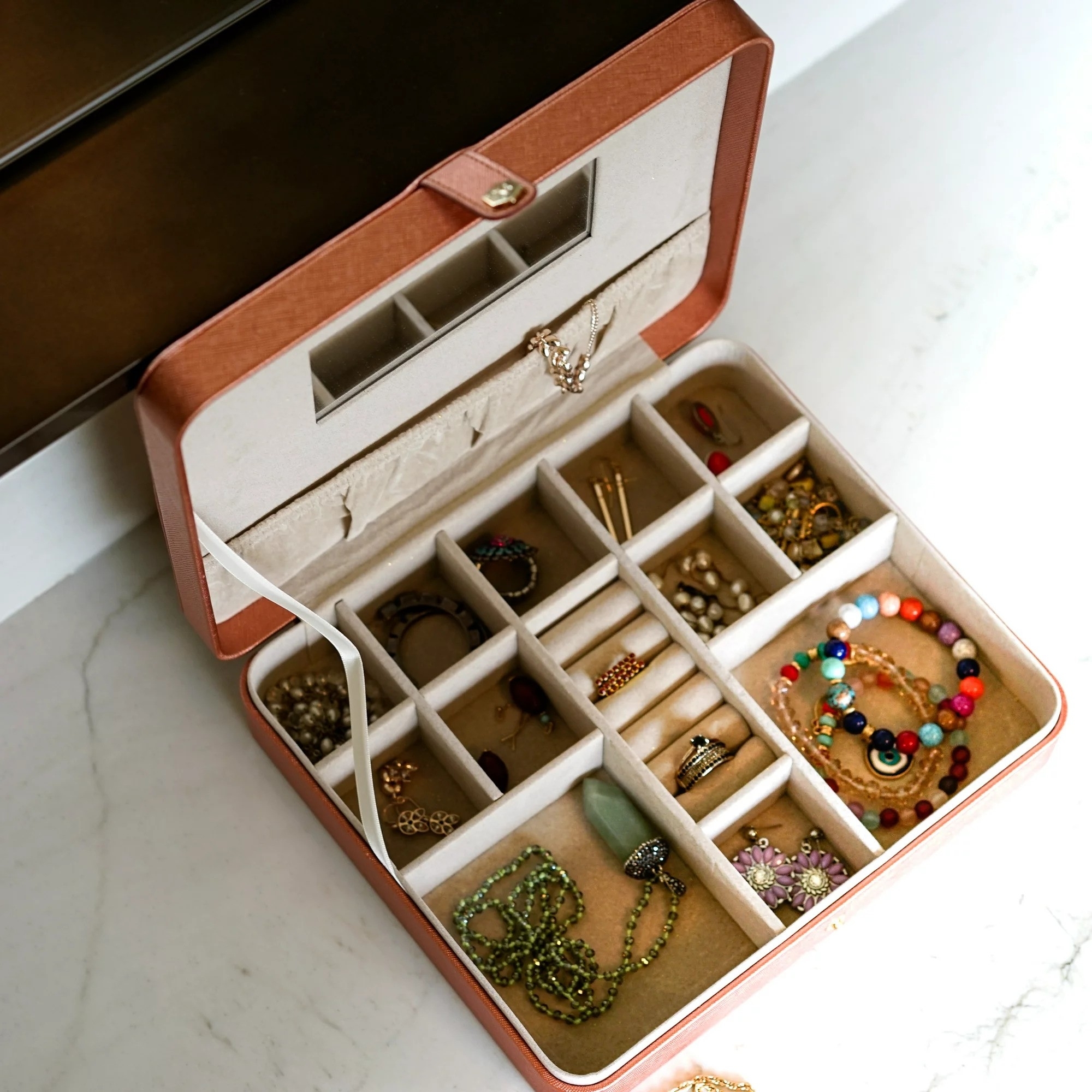 Open jewelry box with various compartments containing necklaces, bracelets, and earrings