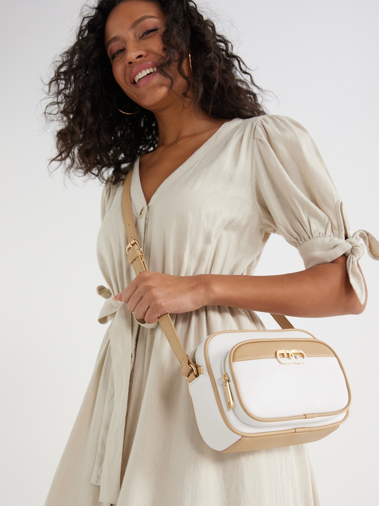 Smiling model in a stylish dress posing with a white crossbody bag