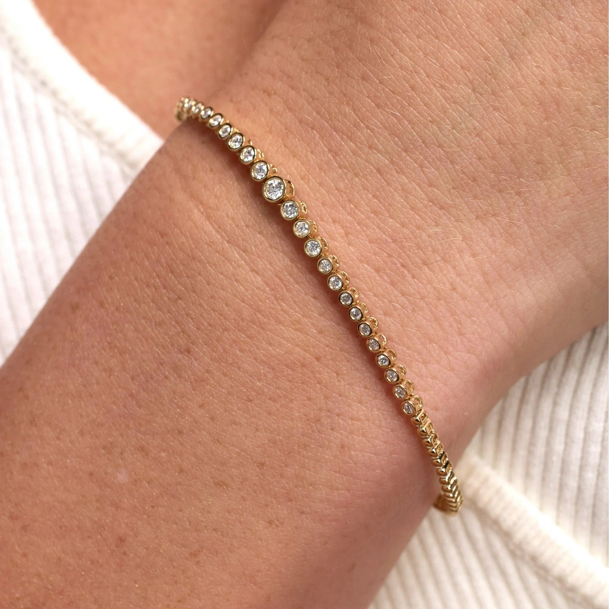 Wrist adorned with a delicate gold tennis bracelet featuring a single row of clear, round diamonds