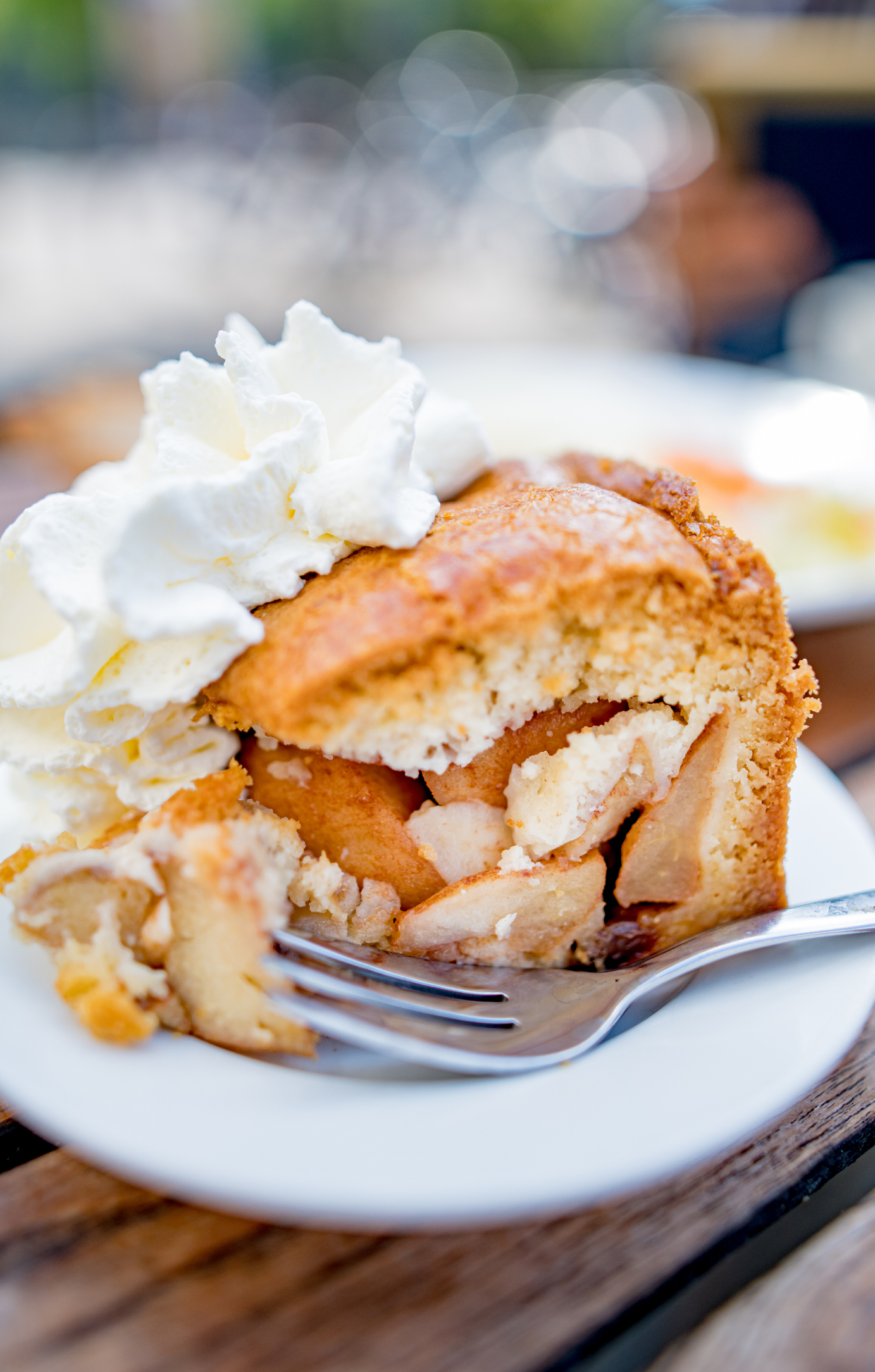 A slice of apple pie topped with whipped cream on a plate with a fork