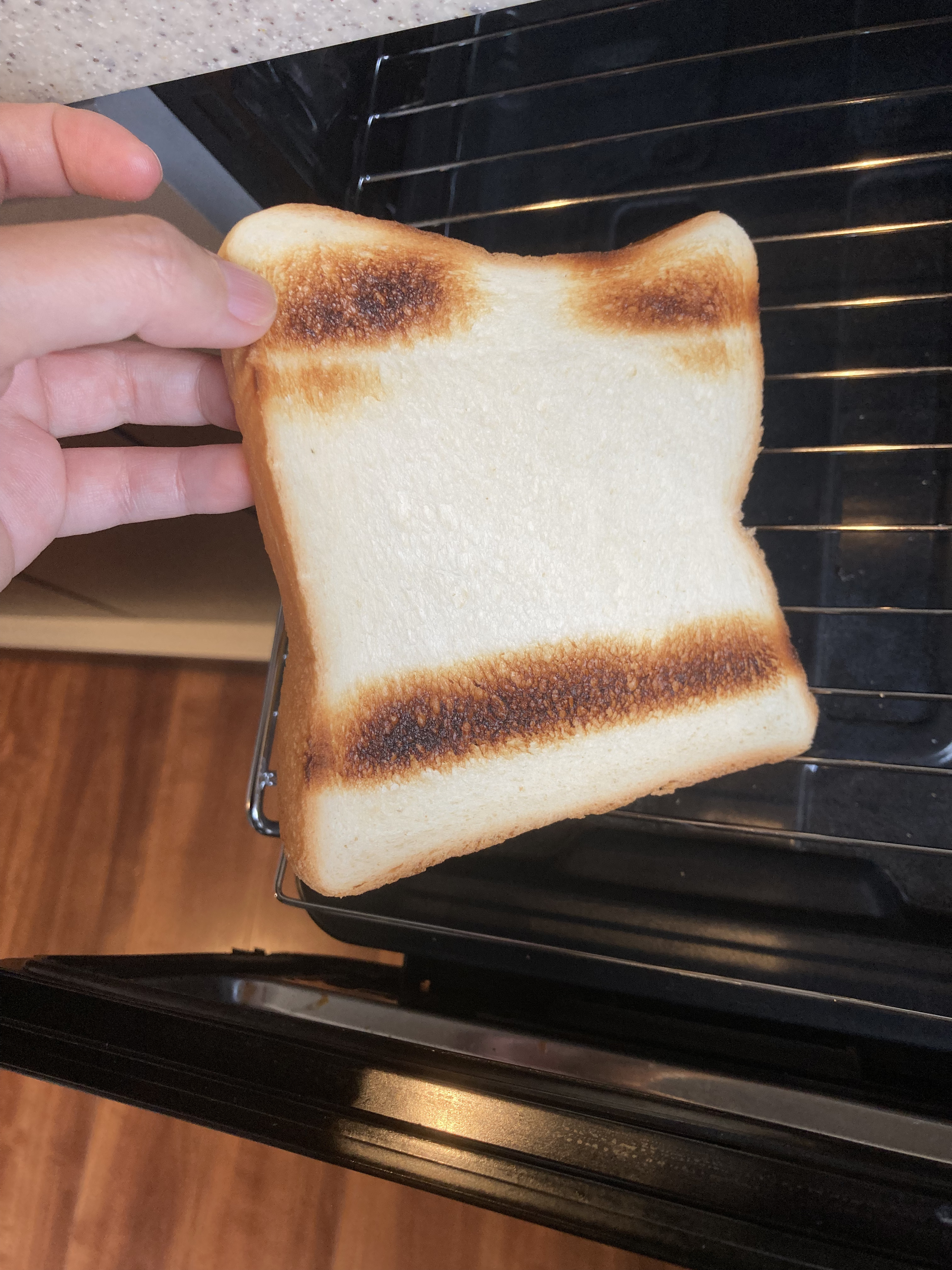 トースターから取り出された片面が焦げたトーストを手が持っている。