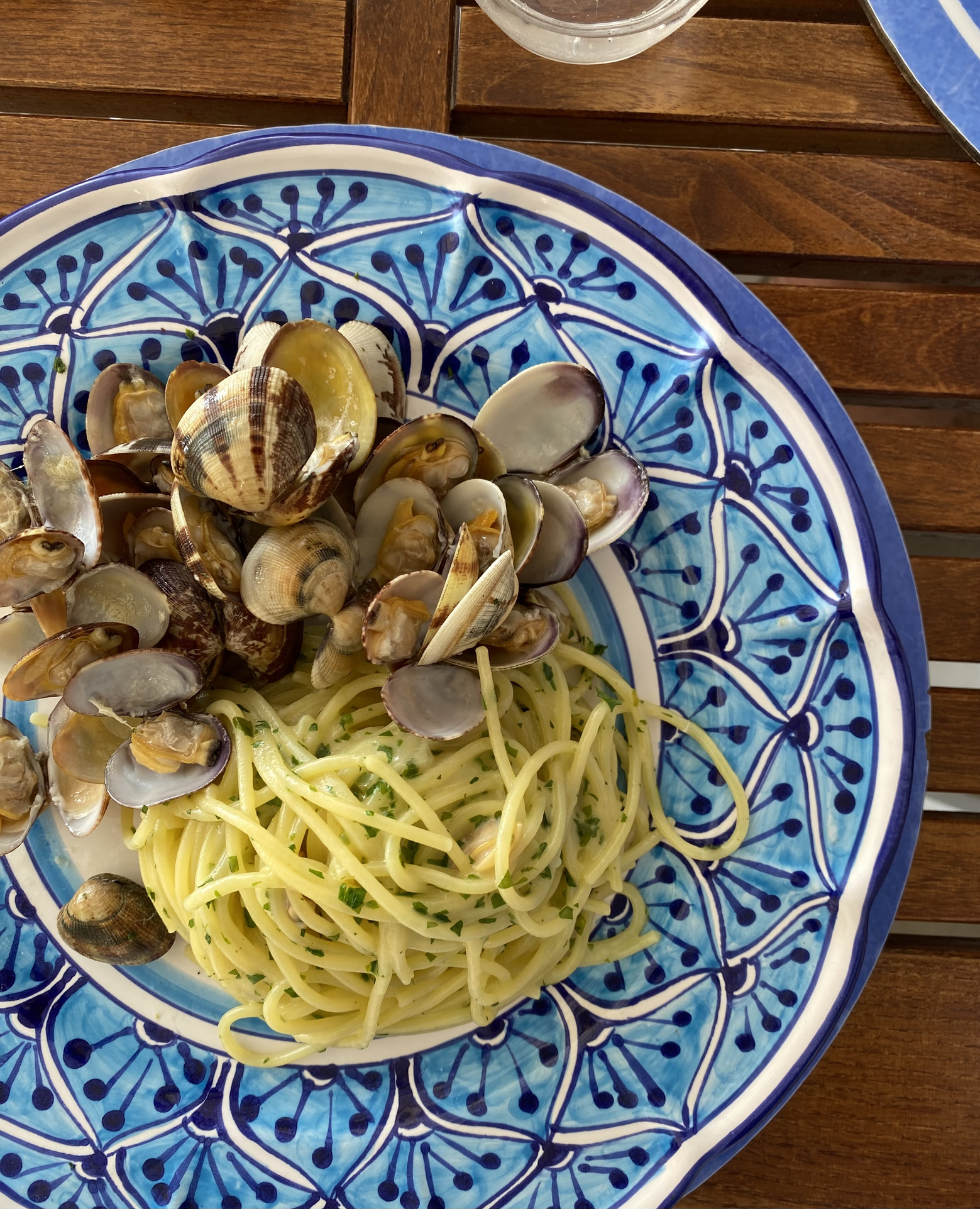 A plate of spaghetti with clams on a patterned plate, set on a wooden table
