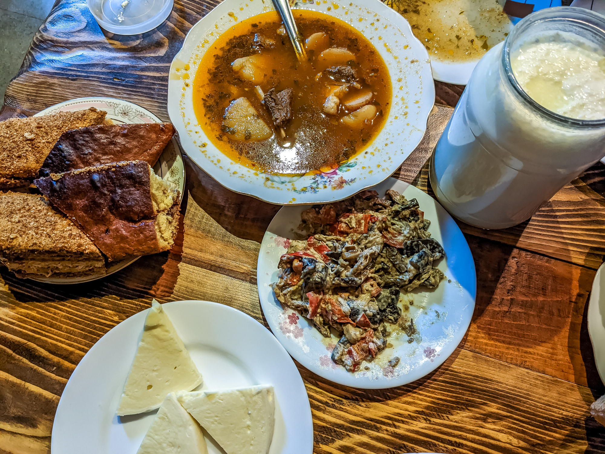Assorted traditional dishes with soup, bread, cheese, and a beverage on a wooden table