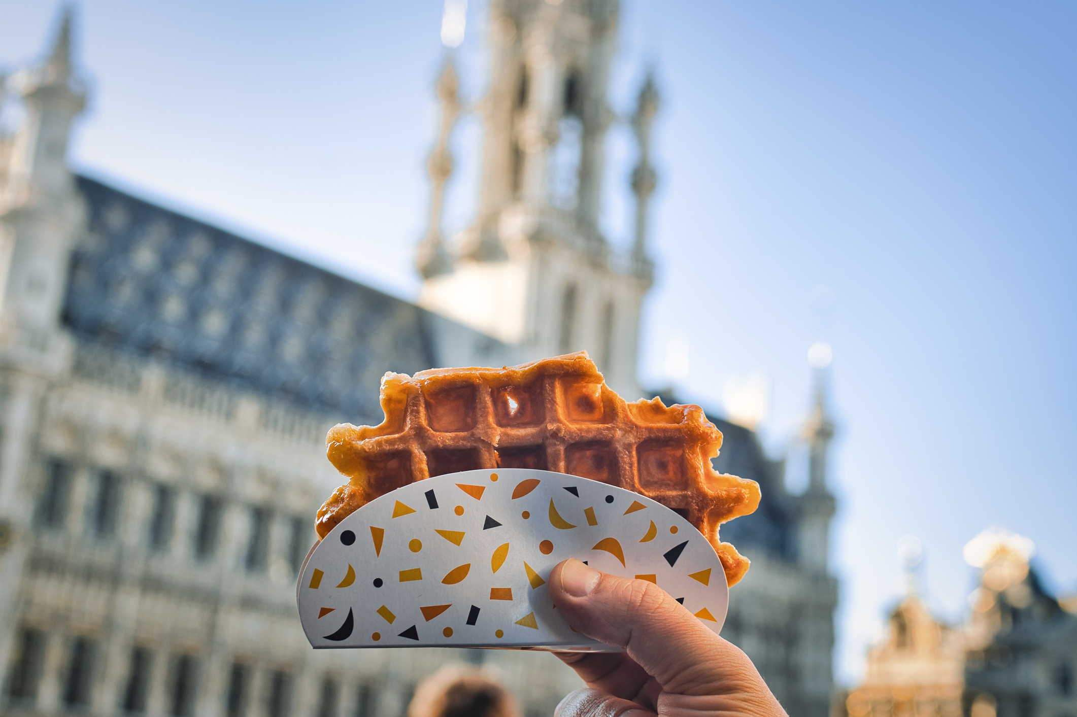 Hand holding a waffle against a backdrop of the Grand Place in Brussels