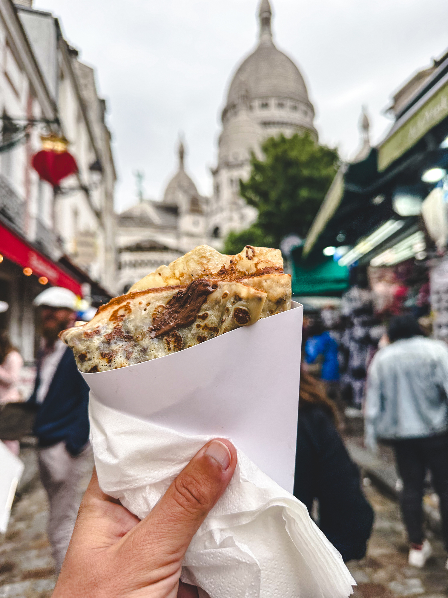 Person holding a crepe with Sacré-Cœur Basilica in the distant background