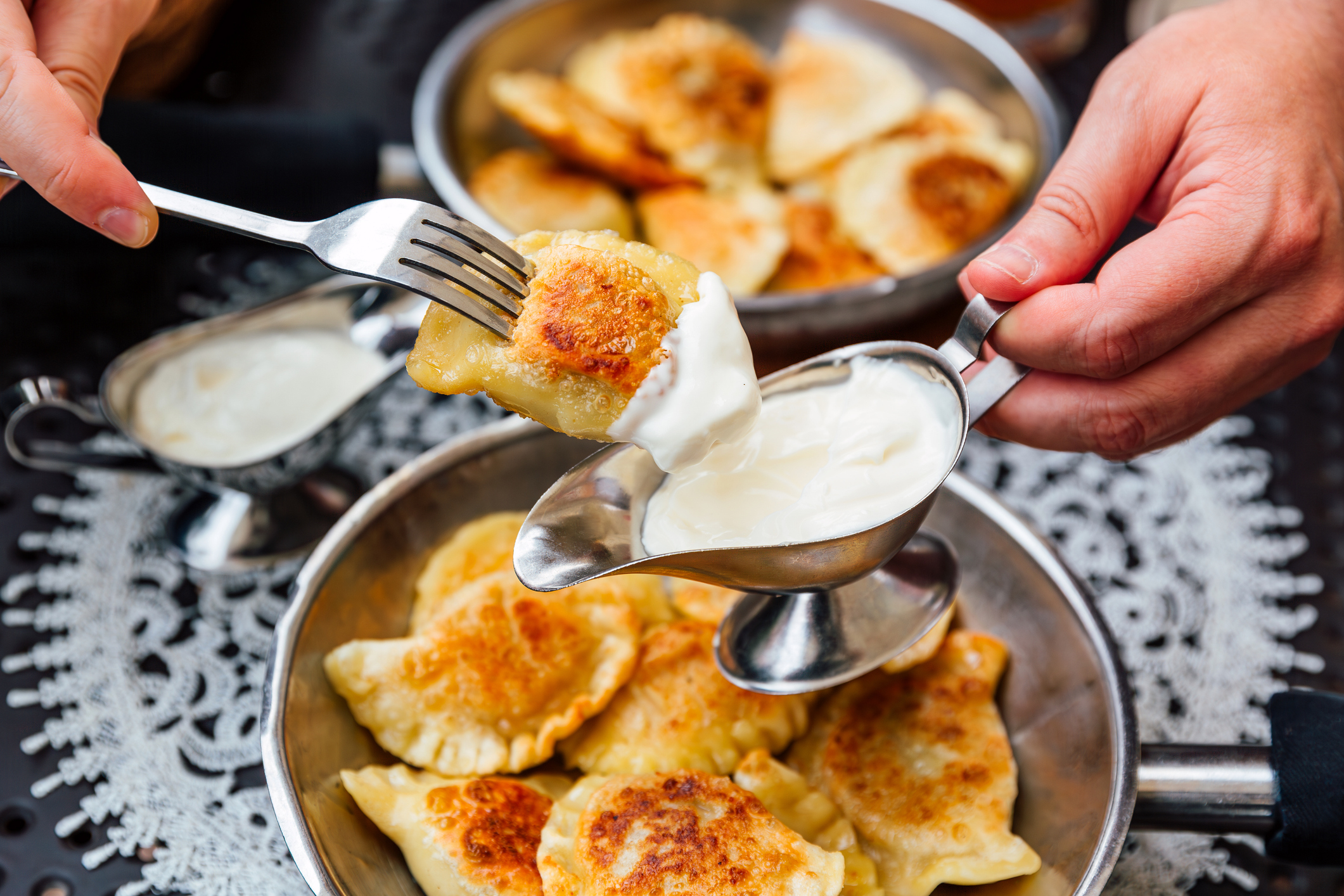 Person serving sour cream onto fried dumplings with a spoon and fork