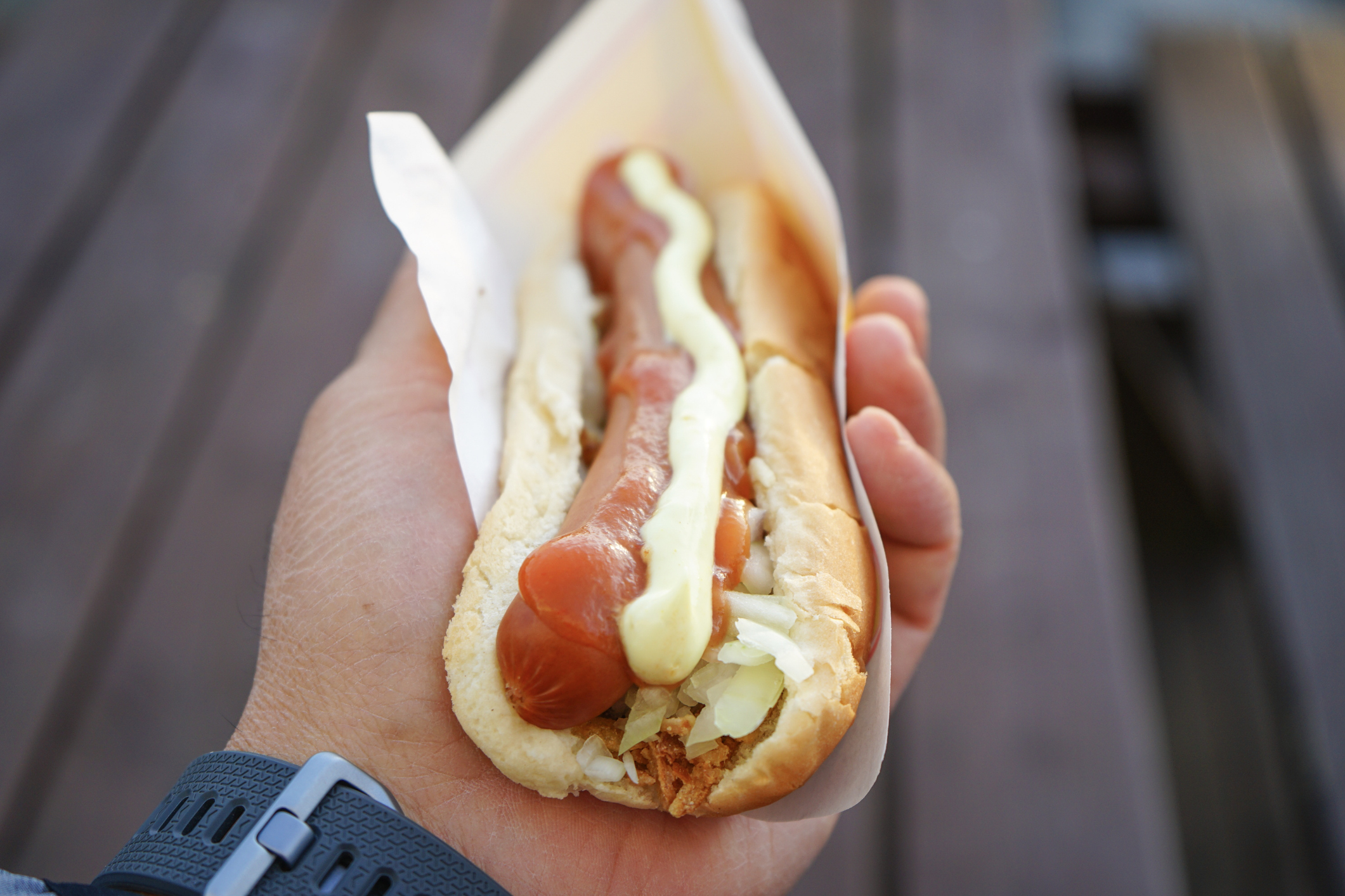 Close-up of a hand holding a hot dog with condiments. No individuals identified
