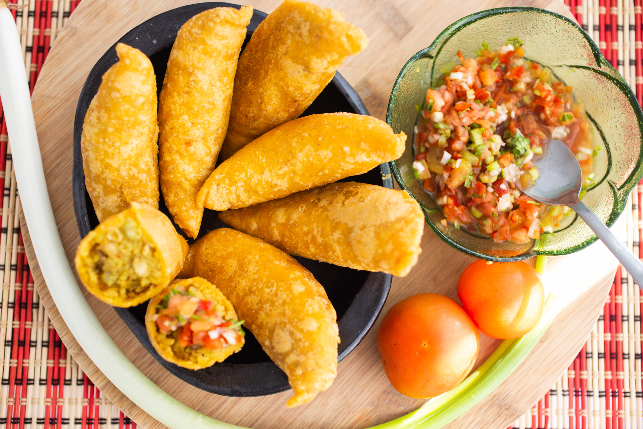 A plate of empanadas with one cut open, alongside a bowl of salsa and fresh tomatoes