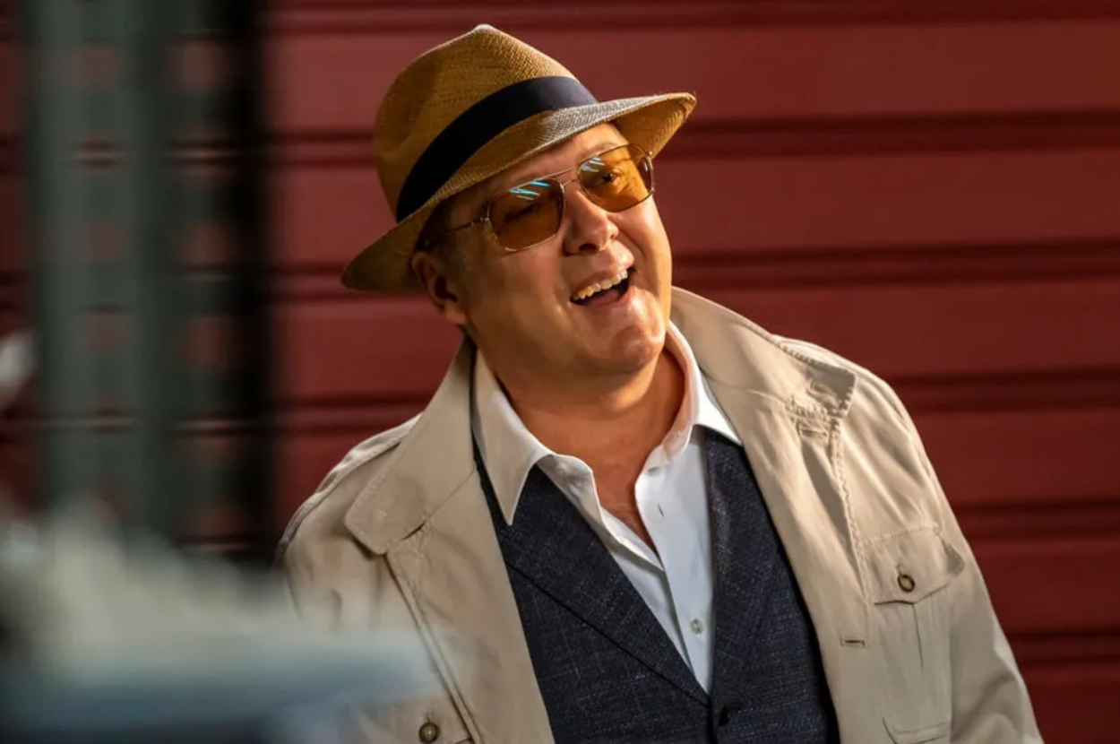 James Spader as Raymond Reddington wearing a fedora and light jacket, smiling in a scene from The Blacklist