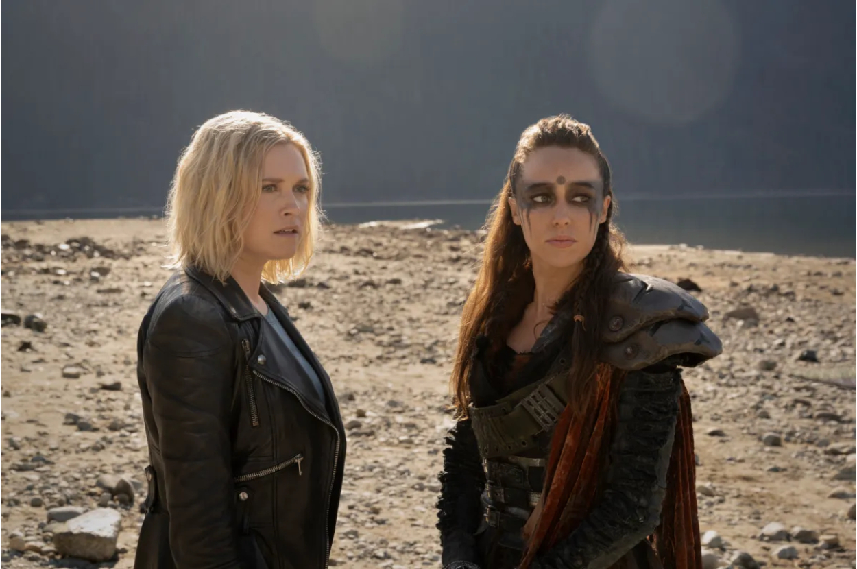 Two characters from a scene in &quot;The 100&quot; TV show standing in a barren landscape, one in leather jacket, other in armor