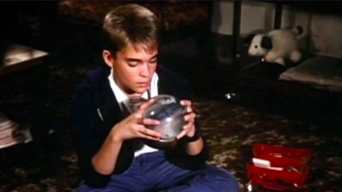Young boy focused on a puzzle sphere in a room with toys scattered around