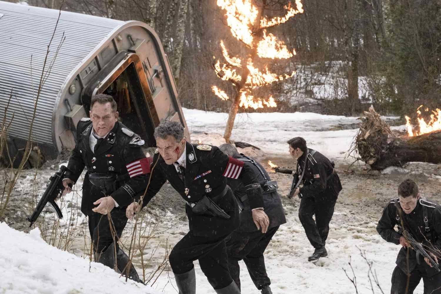 Characters in military uniforms flee an overturned, fiery vehicle in a snowy landscape