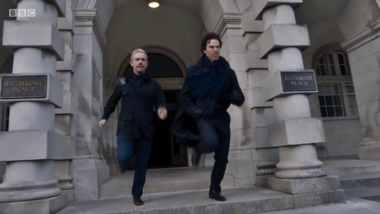 Two characters, John Watson and Sherlock Holmes, from the TV show Sherlock, are running down the steps of Rathbone Place