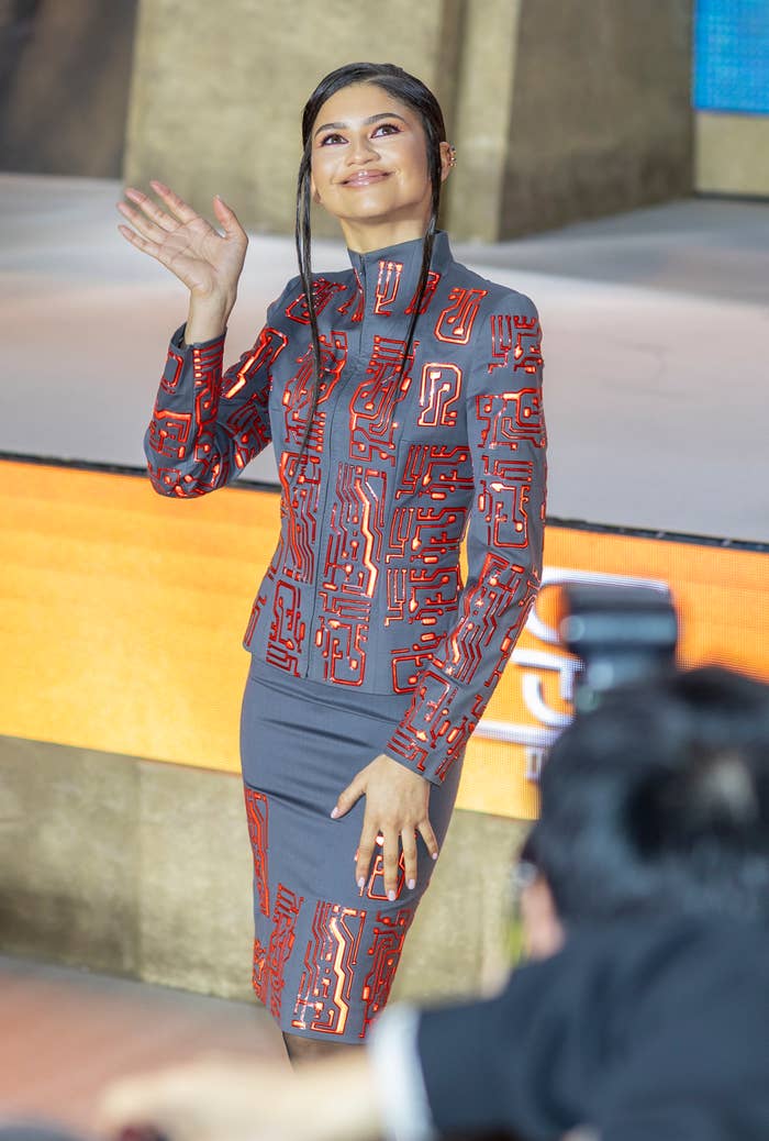 Zendaya waves wearing a patterned high-neck dress at an event