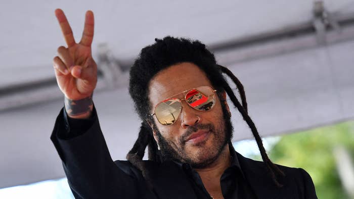 Person with dreadlocks in sunglasses and black outfit flashing a peace sign