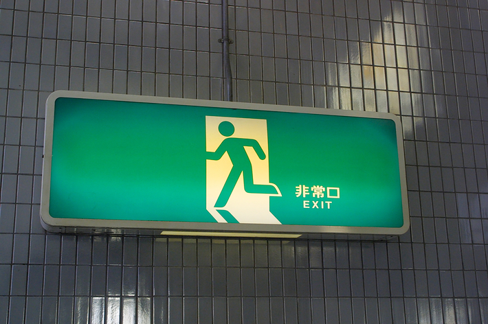 出口を示す看板で、人のシルエットが描かれ、「出口」と「EXIT」と書かれています。