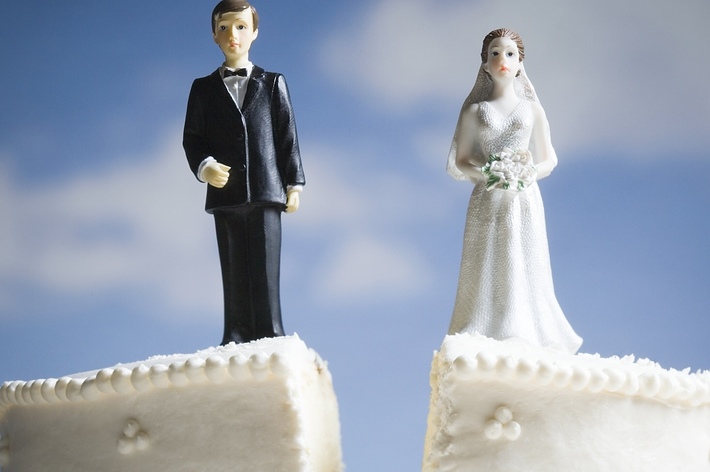 Bride and groom cake toppers on a split wedding cake against a blue backdrop