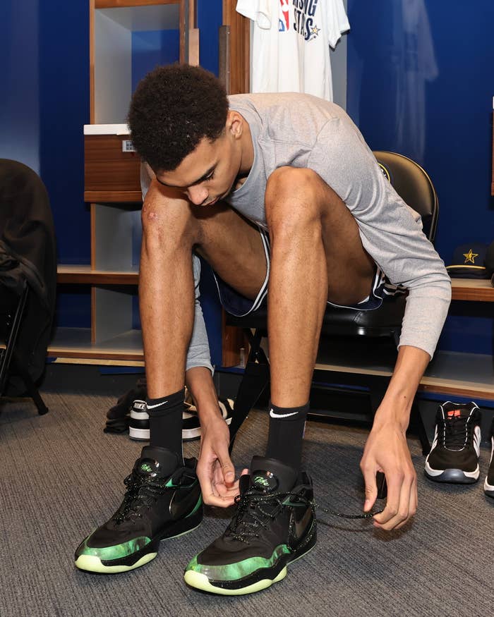 Athlete tying laces of black and green sneakers before a game, sitting in a locker room