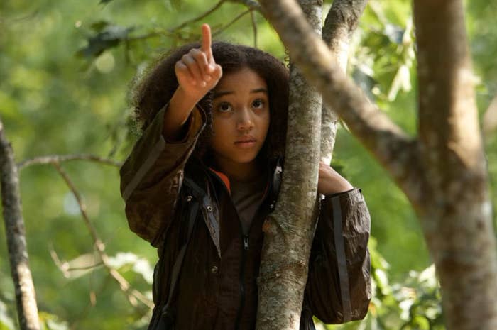 Young girl in a forest, looking cautious with finger raised to lips gesturing silence
