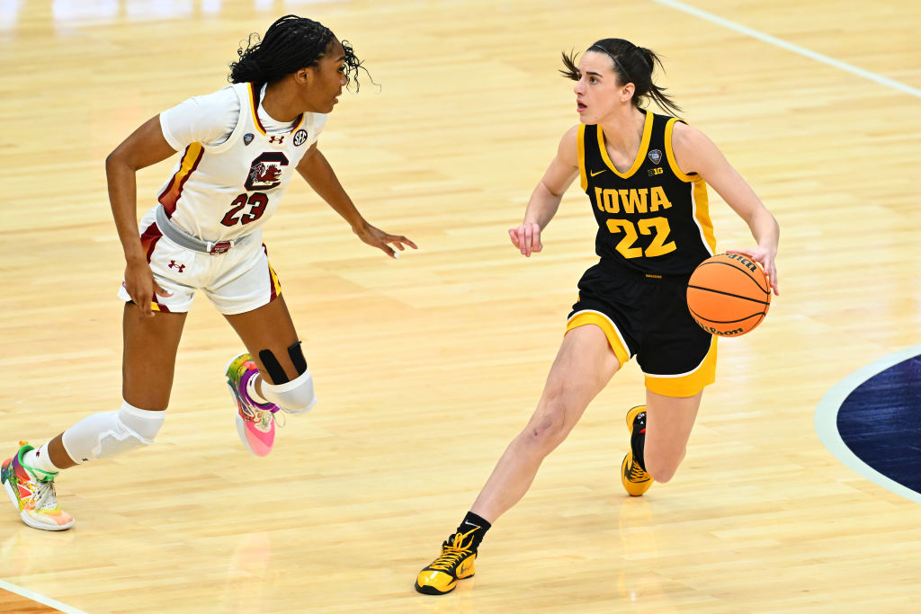 Two basketball players in action, one from Iowa in black and gold, the other from South Carolina in white and maroon