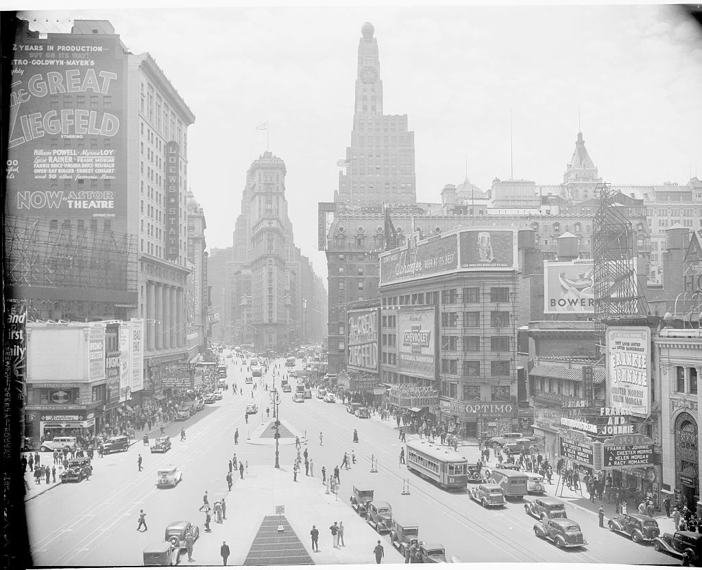 Historic photo of a bustling city street with early 20th-century architecture and numerous vintage signs