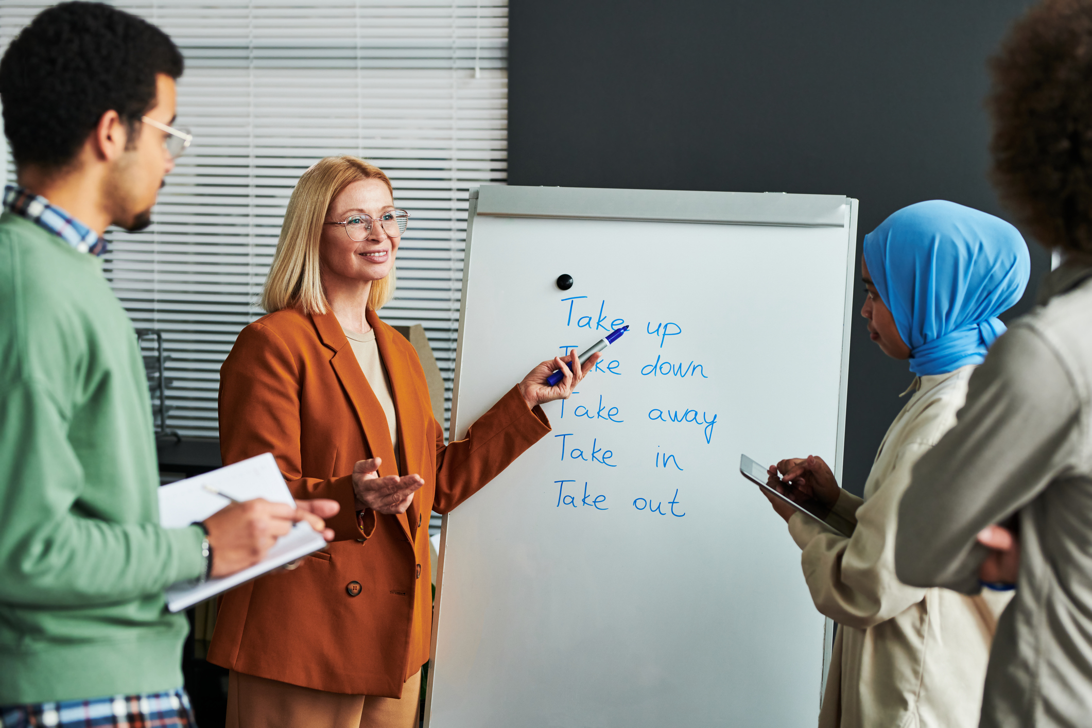 Woman presents on whiteboard to colleagues, in a classroom setting