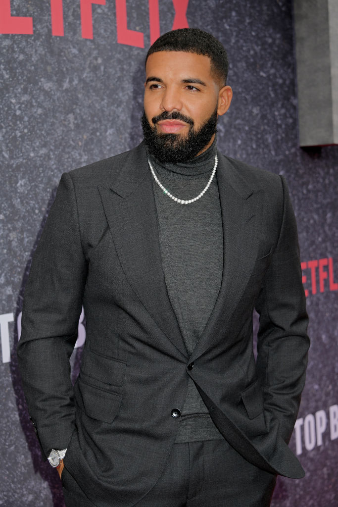 Drake in a fitted suit with a turtleneck and chain, posing at a Netflix event