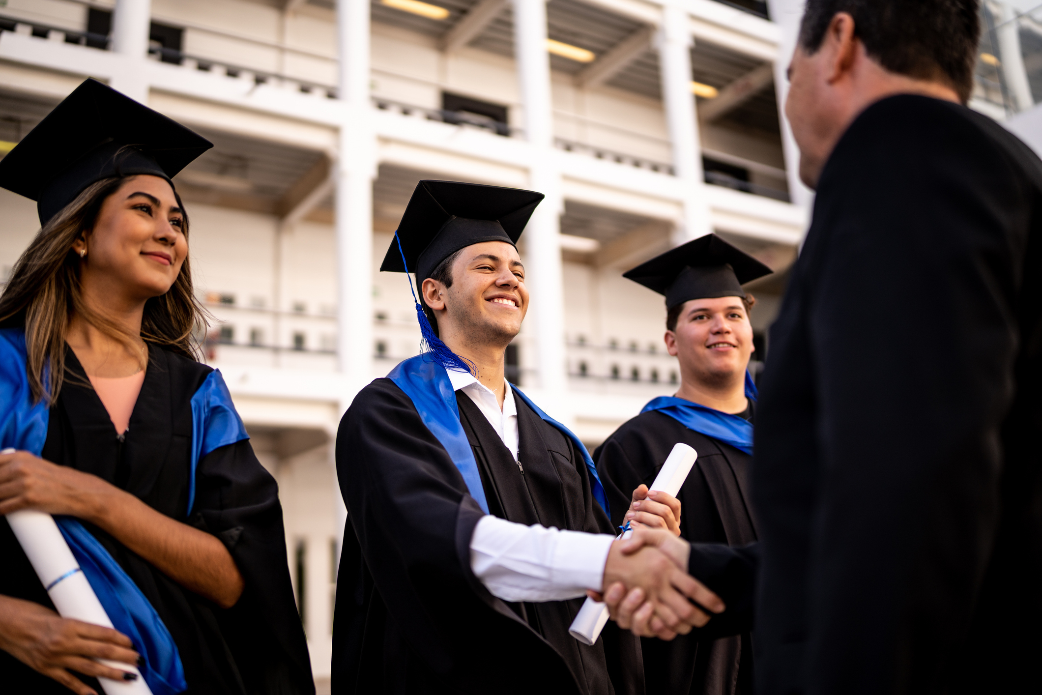 Graduates in cap and gown shaking hands with a faculty member at a graduation ceremony