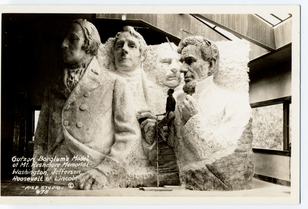 Sculptor Gutzon Borglum&#x27;s model of Mt. Rushmore with Washington, Jefferson, Roosevelt, and Lincoln faces; artist standing beside it