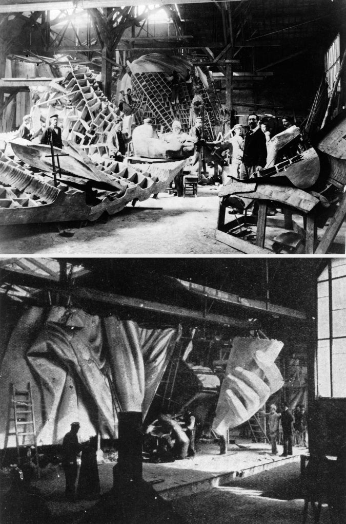 Historical photo of workers constructing the framework of a large ship in an industrial hangar