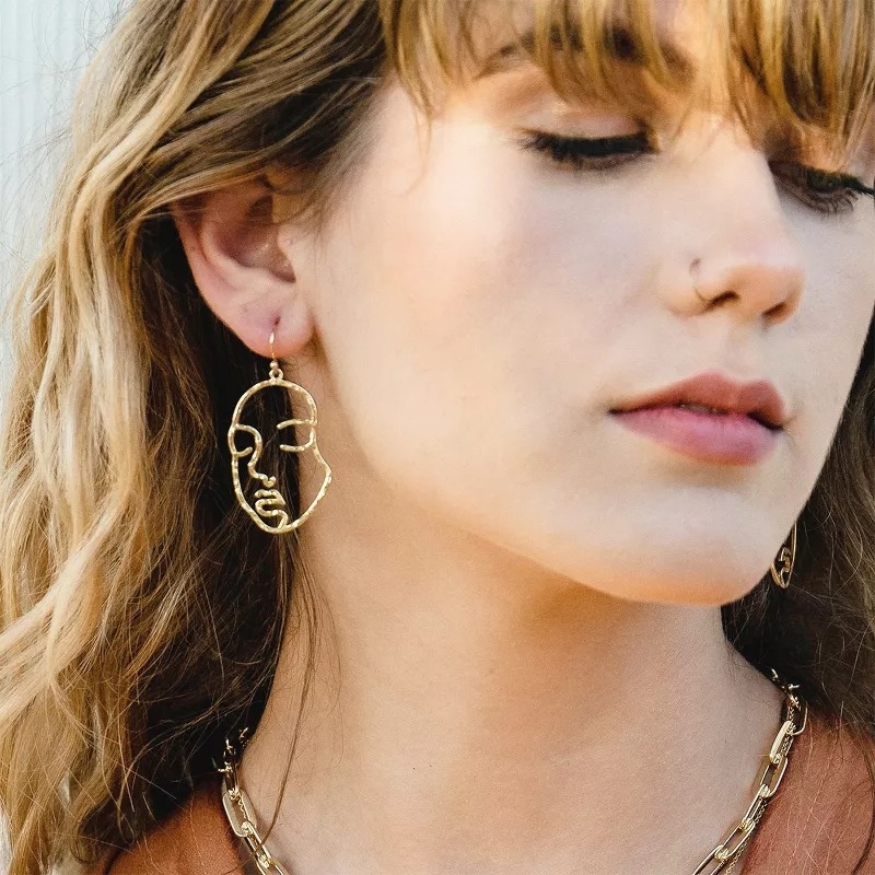 Close-up of a person wearing abstract face-shaped earrings