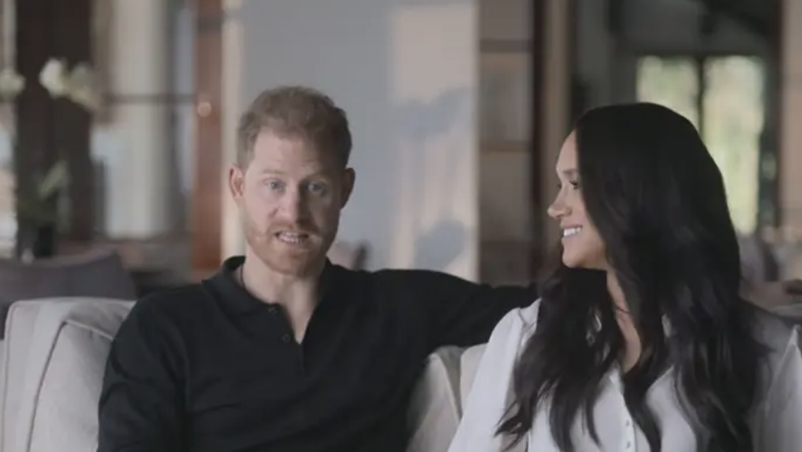 Prince Harry and Meghan Markle sitting together, smiling in a relaxed indoor setting